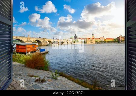 Vue par une fenêtre le long des rives de la Vltava, avec le pont Charles, la vieille ville et la tour du pont de la vieille ville à Prague, la Tchéquie au coucher du soleil. Banque D'Images