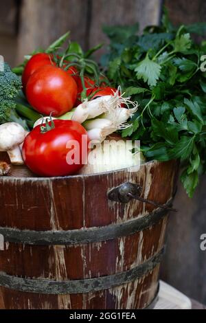 Tomates cueillies à la main, brocoli, oignons verts, persil dans un seau rustique Banque D'Images