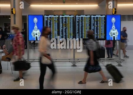 Les personnes ayant un masque facial marchent devant le panneau des départs au terminal nord de l'aéroport international de Seattle-Tacoma, le vendredi 20 août 2021, en mer Banque D'Images