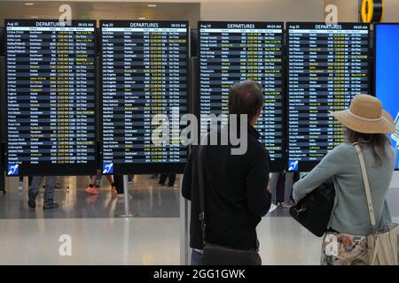 Les personnes avec des masques de visage marchent à côté du panneau des départs au terminal nord de l'aéroport international de Seattle-Tacoma, le vendredi 20 août 2021, in Banque D'Images