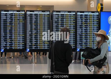 Les personnes avec des masques de visage marchent à côté du panneau des départs au terminal nord de l'aéroport international de Seattle-Tacoma, le vendredi 20 août 2021, in Banque D'Images