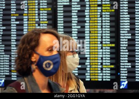 Les personnes ayant un masque facial marchent devant le panneau des départs au terminal nord de l'aéroport international de Seattle-Tacoma, le vendredi 20 août 2021, en mer Banque D'Images