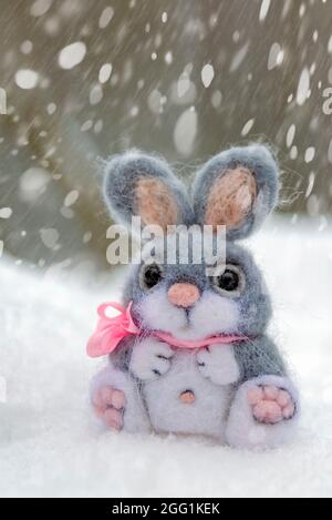 Lapin drôle dans la neige, noël ou pâques concept. Un lièvre gris jouet est  assis dans une dérive de neige sur fond de forêt et de neige tombant. Carte  postale Photo Stock - Alamy