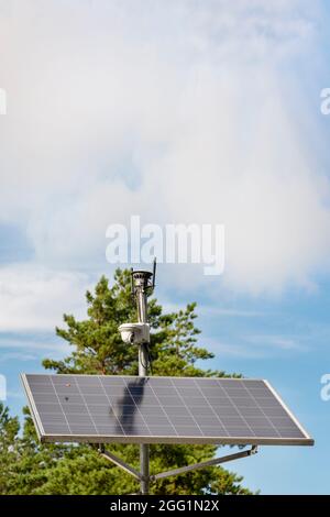 Caméra de surveillance à énergie solaire. Panneaux solaires alimentant une caméra de surveillance dans un parc urbain sur fond de ciel bleu. Sécurité et nettoyage Banque D'Images