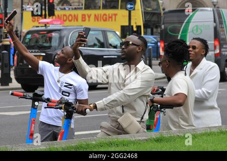 Westminster, Londres, Royaume-Uni. 27 août 2021. Quatre jeunes hommes prennent des photos autour de la place du Parlement et de ses nombreux sites touristiques tout en explorant la région à bord de scooters électroniques. Le centre de Londres revient lentement à l'époque pré-pandémique, avec un nombre croissant de visiteurs, un nombre croissant de personnes visitant la ville, ainsi que de plus en plus de gens s'aventurant dans la ville. Credit: Imagetraceur/Alamy Live News Banque D'Images