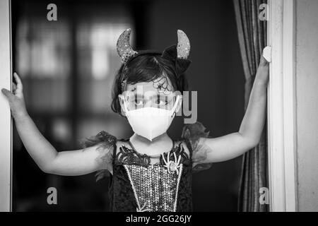 Prise de vue en niveaux de gris d'une fille d'Asie du Sud-est dans un costume d'Halloween et un maquillage portant un masque sanitaire Banque D'Images