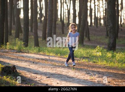 Une fille aux cheveux blonds court le long d'un chemin de forêt sautant sur toutes les branches le matin Banque D'Images