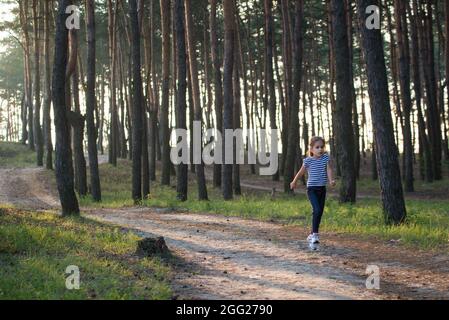 Une fille aux cheveux blonds court le long d'un chemin de forêt sautant sur toutes les branches le matin Banque D'Images