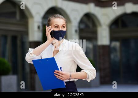 femme d'affaires dans un masque médical parlant au téléphone Banque D'Images