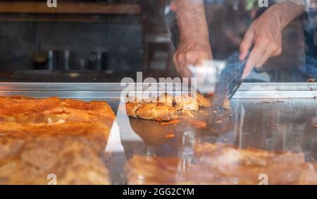 Bougatsa dans une exposition de magasin, Male fait couper les mains pâte avec la viande hachée en morceaux. Petit déjeuner traditionnel avec garniture douce ou salée entre les couches de Banque D'Images