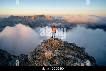 Homme avec sac à dos haut au-dessus de la vallée de montagne brumeux. La personne seule regarde une montagne entourée de brume et de nuages avec le pic visible. SC Banque D'Images