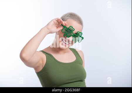 Portrait d'une jeune femme caucasienne avec une coupe de cheveux d'un homme dans un t-shirt vert et des lunettes gaies sur un fond blanc. La jeune fille célèbre St patrick Banque D'Images