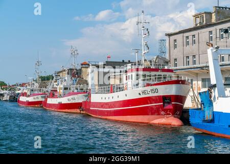 Hel, Pologne - 08.01.2021: Ligne de bateaux de pêche rouges et blancs amarrés à la jetée lors d'une journée ensoleillée d'été avec des bâtiments portuaires en arrière-plan. Banque D'Images