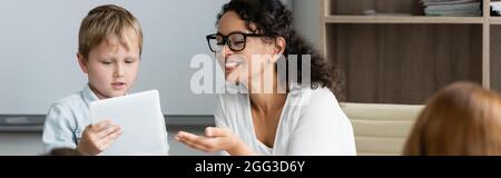 joyeux professeur afro-américain pointant vers une tablette numérique près d'un écolier, bannière Banque D'Images