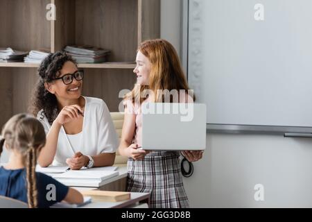 bonne fille avec un ordinateur portable regardant un professeur afro-américain en classe Banque D'Images