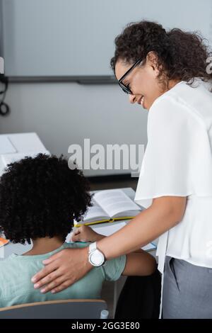 un professeur afro-américain souriant touche l'arrière de l'élève en classe Banque D'Images