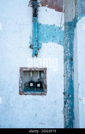 Plan vertical détaillé des anciens fils électriques menant dans une boîte avec des interrupteurs électriques vintage sur un mur blanc, bleu et rouge fissuré. Lieu abandonné Banque D'Images