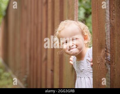 Un gamin drôle en vêtements légers regarde par un trou dans la clôture. Jour ensoleillé d'été. Copier l'espace Banque D'Images