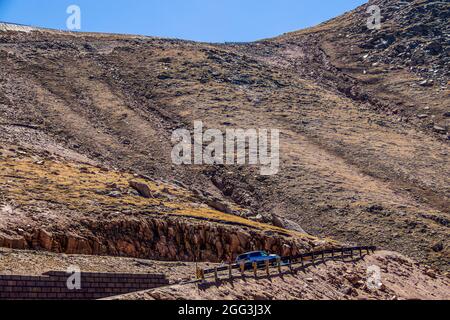 Un SUV et une moto prennent un retour sur une route sinueuse de montagne au-dessus de la ligne des arbres - vous pouvez voir où la route continue sur le sommet de la rigg Banque D'Images