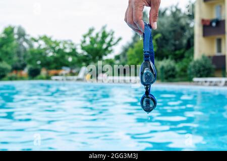 Main de l'homme tenant des lunettes de natation professionnelles avec de l'eau bleu de piscine sur fond Banque D'Images