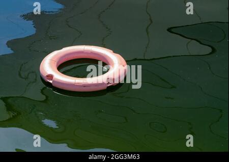 Gros plan d'une bouée de sauvetage rose flottant sur une surface d'eau verte et bleue avec des réflexions créant un motif abstrait enrageant. Concept abstrait de l'aide Banque D'Images