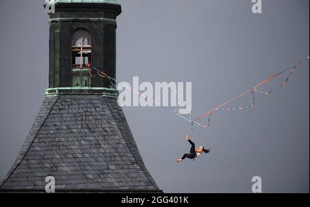 Hohnstein, Allemagne. 28 août 2021. Un coureur de slackline pend sur une corde entre le château et l'église de la ville de la Suisse saxonne à la Highline - et le Festival de la famille. La ligne de démarcation est étirée à 30 mètres au-dessus du marché pour plus de 100 mètres. Un total de 4 cordes sont installées autour du château Hohnstein, le plus long est de 360 mètres de long au-dessus du Polenztal. Credit: Robert Michael/dpa-Zentralbild/dpa/Alay Live News Banque D'Images