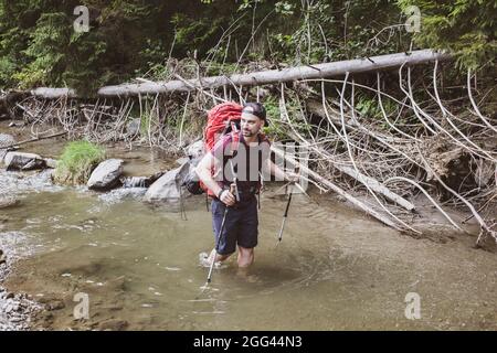 Un randonneur descend la rivière sur ses genoux dans l'eau dans les montagnes, Chyvchyny, frontière ukrainienne-roumaine dans les Carpates Banque D'Images