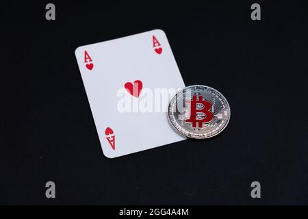 Un argent Bitcoin avec logo sur la couleur rouge, menti sur la carte à jouer rouge ace sur le bureau avec fond sombre. Technologie numérique et de virtualisation la plus populaire de BTC Banque D'Images