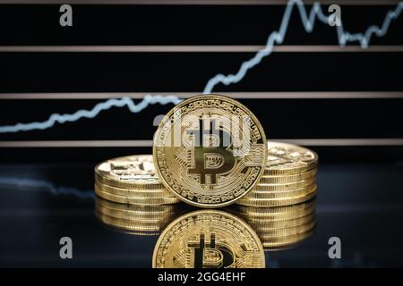 Gros plan de la pièce physique Bitcoin, devant un tableau de prix Banque D'Images