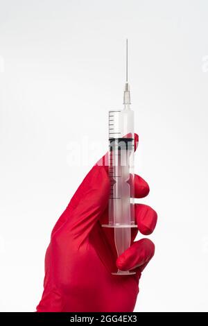 Médecin mains dans des gants médicaux rouges tenant une seringue médicale pour injection de vaccin sur fond blanc. Concept médical d'immunisation et de vaccination Banque D'Images