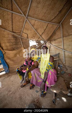 Tolofidje Mariam (26, C) est assise avec sa fille Damango Awa (2, L) et sa mère, Togo Awa (45, R), à l'intérieur de la tente improvisée où ils dorment. La famille a fui son village d'origine en raison de la violence et de l'insécurité. Parce qu'ils ne peuvent pas cultiver, ils font face à la faim et à des pénuries alimentaires chaque jour. Crise du Sahel 2021; province du Kossi, Burkina Faso. 18 févr. 2021. Photo de Jake Lyell. Banque D'Images