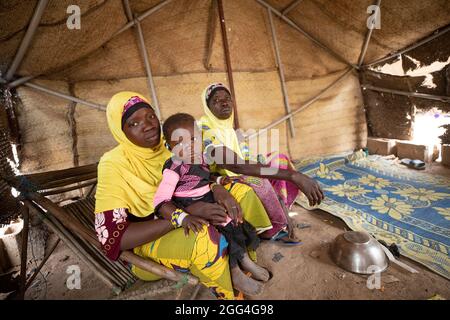 Tolofidje Mariam (26, L) est assise avec sa fille Damango Awa (2, C) et sa mère, Togo Awa (45, R), à l'intérieur de la tente improvisée où ils dorment. La famille a fui son village d'origine en raison de la violence et de l'insécurité. Parce qu'ils ne peuvent pas cultiver, ils font face à la faim et à des pénuries alimentaires chaque jour. Crise du Sahel 2021; province du Kossi, Burkina Faso. 18 févr. 2021. Photo de Jake Lyell. Banque D'Images