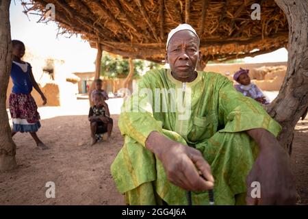 Mahammoud Traore (75) soutient une famille de 21 personnes grâce à son agriculture dans le village de Dougouninkoro, au Mali. Mais le changement climatique a affecté les tendances météorologiques ces dernières années et il n'a pas été capable de croître autant qu'il l'avait fait auparavant. Aujourd’hui, les réserves alimentaires de sa famille sont toujours à court de nourriture avant de pouvoir récolter sa nouvelle récolte. Par conséquent, il y a toujours deux mois chaque année où la famille fait l’expérience de la faim et qu’ils doivent souvent s’endetter pour acheter ou emprunter de la nourriture. Crise du Sahel 2021 ; Barouéli cercle, Mali. 22 févr. 2021. Photo de Jake Lyell. Banque D'Images