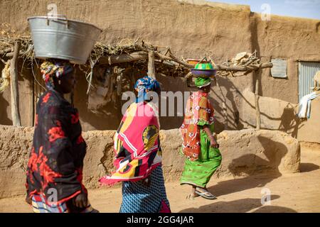 Mahammoud Traore (75) soutient une famille de 21 personnes grâce à son agriculture dans le village de Dougouninkoro, au Mali. Mais le changement climatique a affecté les tendances météorologiques ces dernières années et il n'a pas été capable de croître autant qu'il l'avait fait auparavant. Aujourd’hui, les réserves alimentaires de sa famille sont toujours à court de nourriture avant de pouvoir récolter sa nouvelle récolte. Par conséquent, il y a toujours deux mois chaque année où la famille fait l’expérience de la faim et qu’ils doivent souvent s’endetter pour acheter ou emprunter de la nourriture. Ici, plusieurs membres de M. Traore portent des tenues colorées lorsqu'ils traversent leur composition familiale. Crise du Sahel 2021 ; Barouéli Banque D'Images