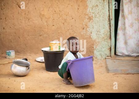 Mahammoud Traore (75, non représenté) soutient une famille de 21 personnes grâce à son agriculture dans le village de Dougouninkoro, Mali. Mais le changement climatique a affecté les tendances météorologiques ces dernières années et il n'a pas été capable de croître autant qu'il l'avait fait auparavant. Aujourd’hui, les réserves alimentaires de sa famille sont toujours à court de nourriture avant de pouvoir récolter sa nouvelle récolte. Par conséquent, il y a toujours deux mois chaque année où la famille fait l’expérience de la faim et qu’ils doivent souvent s’endetter pour acheter ou emprunter de la nourriture. Ici, le petit-fils de M. Traore, Yaya (2), est assis à l’extérieur du domicile de sa famille. Crise du Sahel 2021 ; Barouéli cercle, Mali. Fév Banque D'Images