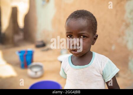 Mahammoud Traore (75, non représenté) soutient une famille de 21 personnes grâce à son agriculture dans le village de Dougouninkoro, Mali. Mais le changement climatique a affecté les tendances météorologiques ces dernières années et il n'a pas été capable de croître autant qu'il l'avait fait auparavant. Aujourd’hui, les réserves alimentaires de sa famille sont toujours à court de nourriture avant de pouvoir récolter sa nouvelle récolte. Par conséquent, il y a toujours deux mois chaque année où la famille fait l’expérience de la faim et qu’ils doivent souvent s’endetter pour acheter ou emprunter de la nourriture. Ici, le petit-fils de M. Traore, Yaya (2), se tient en dehors du domicile de sa famille. Crise du Sahel 2021 ; Barouéli cercle, Mali. F Banque D'Images