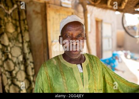 Mahammoud Traore (75) soutient une famille de 21 personnes grâce à son agriculture dans le village de Dougouninkoro, au Mali. Mais le changement climatique a affecté les tendances météorologiques ces dernières années et il n'a pas été capable de croître autant qu'il l'avait fait auparavant. Aujourd’hui, les réserves alimentaires de sa famille sont toujours à court de nourriture avant de pouvoir récolter sa nouvelle récolte. Par conséquent, il y a toujours deux mois chaque année où la famille fait l’expérience de la faim et qu’ils doivent souvent s’endetter pour acheter ou emprunter de la nourriture. Crise du Sahel 2021 ; Barouéli cercle, Mali. 22 févr. 2021. Photo de Jake Lyell. Banque D'Images