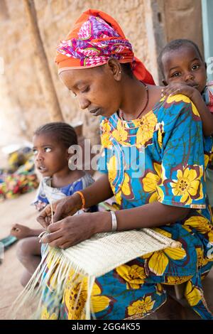 Une mère Fulani déménage à la main des matts et des fans de palmier séché pour assurer la subsistance de sa famille dans la région de Ségou, Mali, Afrique de l'Ouest. Banque D'Images