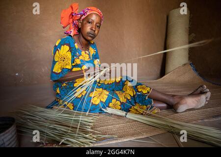 Une femme Fulani déménage à la main des matts et des fans de palmier séché pour la subsistance de sa famille dans la région de Ségou, Mali, Afrique de l'Ouest. Banque D'Images