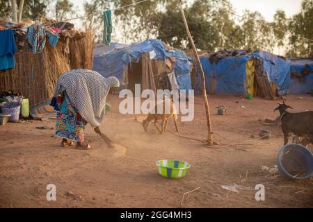 Le camp de Senou se trouve à la limite sud de Bamako, la capitale du Mali. C'est l'un des huit camps informels autour de la ville et, en soi, il abrite 223 familles et un peu plus de 1 000 personnes déplacées. Les familles qui vivent ici ont fui la violence et l'insurrection dans le nord et le centre du pays. Parce que la plupart d'entre eux n'ont pas de moyens de revenu ou de source régulière de nourriture, la faim est un défi quotidien et la malnutrition de sa population reste endémique. Ici, Fatima Bolly (33) balaie la région à l’extérieur du refuge de sa famille tôt le matin. Banque D'Images