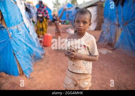 Le camp de Senou se trouve à la limite sud de Bamako, la capitale du Mali. C'est l'un des huit camps informels autour de la ville et, en soi, il abrite 223 familles et un peu plus de 1 000 personnes déplacées. Les familles qui vivent ici ont fui la violence et l'insurrection dans le nord et le centre du pays. Parce que la plupart d'entre eux n'ont pas de moyens de revenu ou de source régulière de nourriture, la faim est un défi quotidien et la malnutrition de sa population reste endémique. Ici, Saido Diallo, âgé de sept ans, se tient à l'extérieur du refuge de sa famille. Banque D'Images