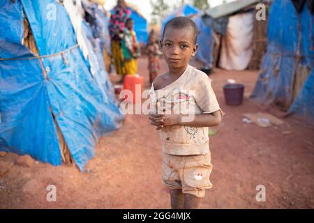 Le camp de Senou se trouve à la limite sud de Bamako, la capitale du Mali. C'est l'un des huit camps informels autour de la ville et, en soi, il abrite 223 familles et un peu plus de 1 000 personnes déplacées. Les familles qui vivent ici ont fui la violence et l'insurrection dans le nord et le centre du pays. Parce que la plupart d'entre eux n'ont pas de moyens de revenu ou de source régulière de nourriture, la faim est un défi quotidien et la malnutrition de sa population reste endémique. Ici, Saido Diallo, âgé de sept ans, se tient à l'extérieur du refuge de sa famille. Banque D'Images