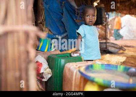 Le camp de Senou se trouve à la limite sud de Bamako, la capitale du Mali. C'est l'un des huit camps informels autour de la ville et, en soi, il abrite 223 familles et un peu plus de 1 000 personnes déplacées. Les familles qui vivent ici ont fui la violence et l'insurrection dans le nord et le centre du pays. Parce que la plupart d'entre eux n'ont pas de moyens de revenu ou de source régulière de nourriture, la faim est un défi quotidien et la malnutrition de sa population reste endémique. Ici, le garçon de deux ans, Bourra Cisse, se tient dans le refuge de fortune de sa famille. Banque D'Images