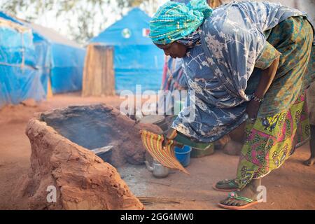 Le camp de Senou se trouve à la limite sud de Bamako, la capitale du Mali. C'est l'un des huit camps informels autour de la ville et, en soi, il abrite 223 familles et un peu plus de 1 000 personnes déplacées. Les familles qui vivent ici ont fui la violence et l'insurrection dans le nord et le centre du pays. Parce que la plupart d'entre eux n'ont pas de moyens de revenu ou de source régulière de nourriture, la faim est un défi quotidien et la malnutrition de sa population reste endémique. Ici, Miriam Barry a un feu avant de cuisiner le petit déjeuner pour sa famille à l'extérieur de leur abri de fortune le matin. Banque D'Images