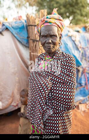 Le camp de Senou se trouve à la limite sud de Bamako, la capitale du Mali. C'est l'un des huit camps informels autour de la ville et, en soi, il abrite 223 familles et un peu plus de 1 000 personnes déplacées. Les familles qui vivent ici ont fui la violence et l'insurrection dans le nord et le centre du pays. Parce que la plupart d'entre eux n'ont pas de moyens de revenu ou de source régulière de nourriture, la faim est un défi quotidien et la malnutrition de sa population reste endémique. Ici, Fatima Barry se tient à l’extérieur du refuge de fortune de sa famille. Banque D'Images