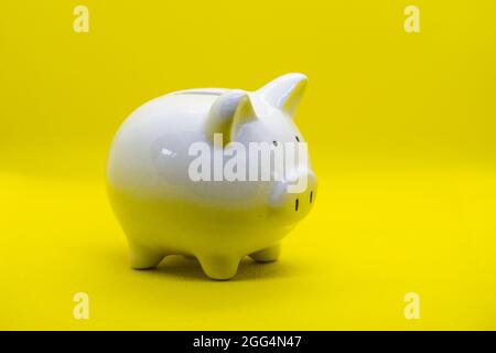 White piggy Bank sur un fond jaune et la main humaine mettant la pièce dans la banque piggy pour économiser l'argent richesse et la finance concept et le copyspace pour de Banque D'Images