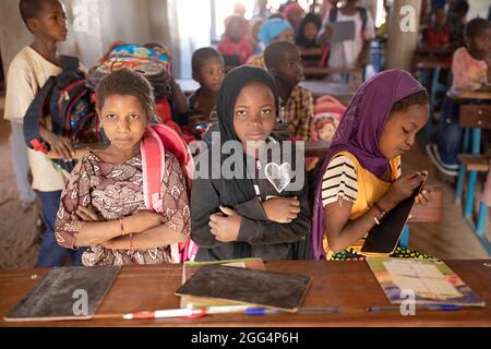 Le camp de Senou se trouve à la limite sud de Bamako, la capitale du Mali. C'est l'un des huit camps informels autour de la ville et, en soi, il abrite 223 familles et un peu plus de 1 000 personnes déplacées. Les familles qui vivent ici ont fui la violence et l'insurrection dans le nord et le centre du pays. Parce que la plupart d'entre eux n'ont pas de moyens de revenu ou de source régulière de nourriture, la faim est un défi quotidien et la malnutrition de sa population reste endémique. Ici, les enfants écrivent sur des lattes de craie dans la seule école primaire du camp, enseignée par Mme Asmatou Coulibably. Banque D'Images