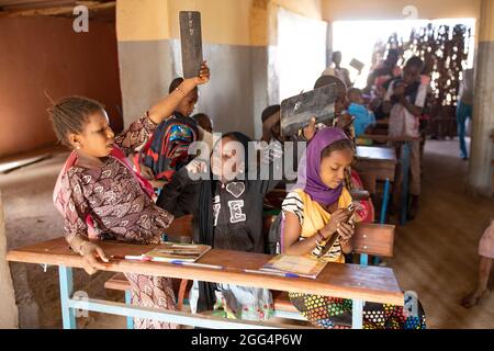 Le camp de Senou se trouve à la limite sud de Bamako, la capitale du Mali. C'est l'un des huit camps informels autour de la ville et, en soi, il abrite 223 familles et un peu plus de 1 000 personnes déplacées. Les familles qui vivent ici ont fui la violence et l'insurrection dans le nord et le centre du pays. Parce que la plupart d'entre eux n'ont pas de moyens de revenu ou de source régulière de nourriture, la faim est un défi quotidien et la malnutrition de sa population reste endémique. Ici, les enfants écrivent sur des lattes de craie dans la seule école primaire du camp, enseignée par Mme Asmatou Coulibably. Banque D'Images