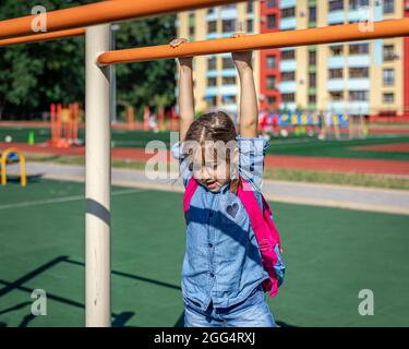 Une petite fille, une étudiante à l'école primaire, joue sur le terrain de jeu après l'école, se lève sur une barre horizontale. Banque D'Images