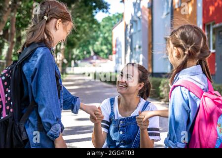 Une jeune femme soutient moralement les filles qui tiennent la main encourage les enfants, accompagne les élèves à l'école. Banque D'Images